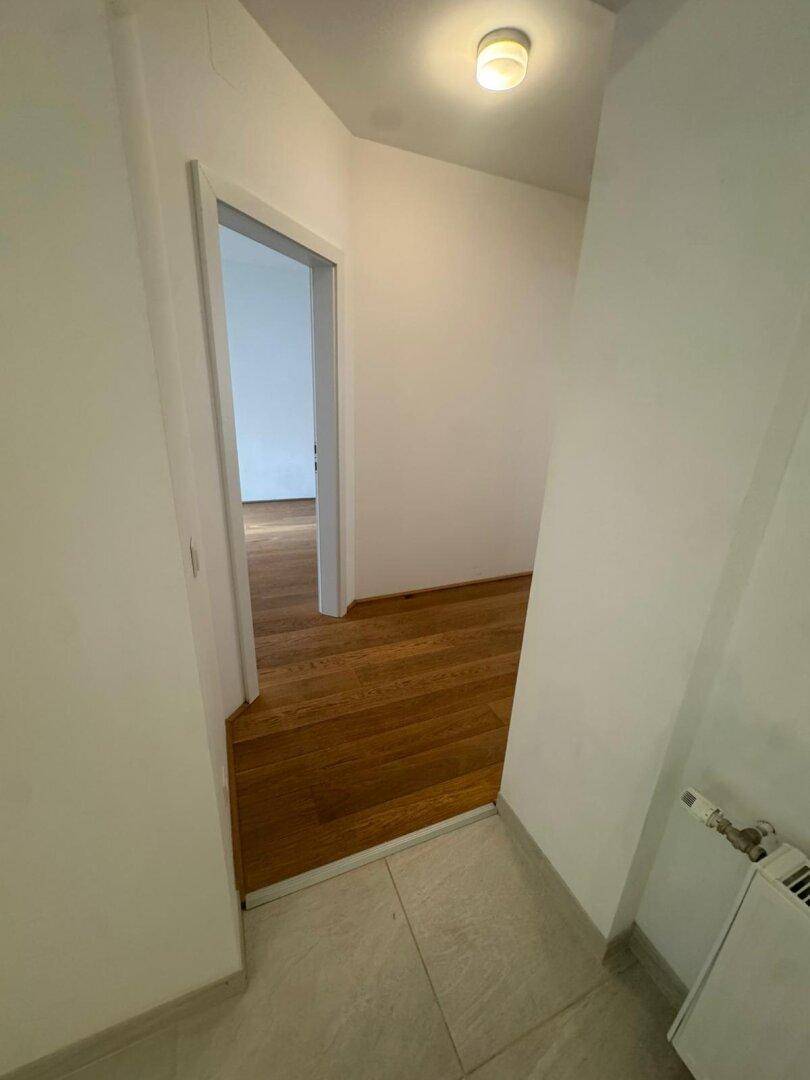 Übergang von einem gefliesten Flur in einen Raum mit neuem Hartholzboden und Heizkörper.