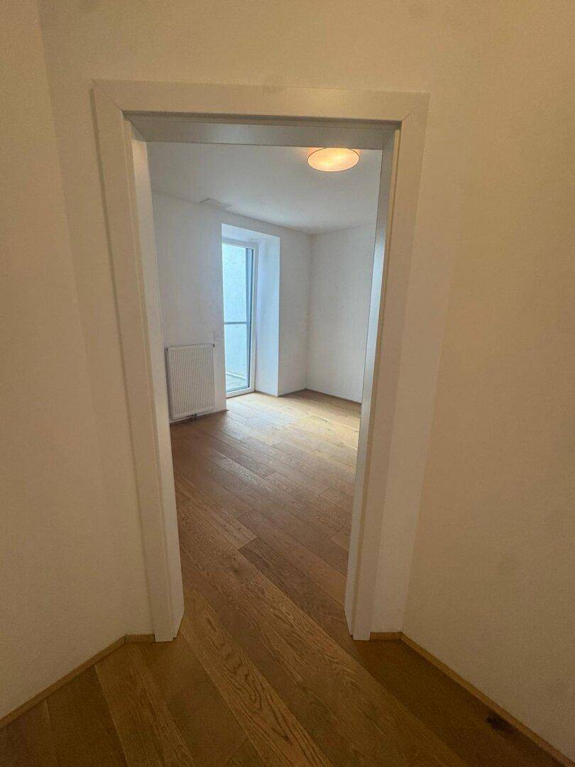 Blick von einem gefliesten Flur in ein Zimmer mit elegantem Hartholzboden und heller Beleuchtung.