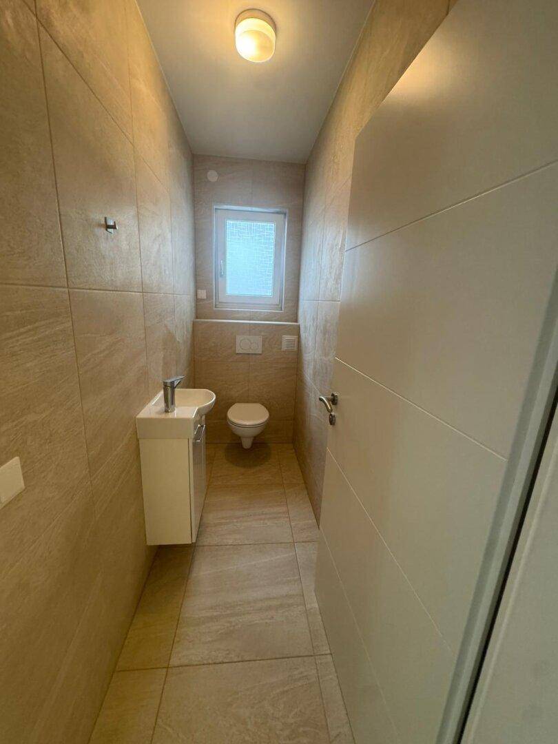 Modernes Gäste-WC mit beigefarbenen Fliesen, wandhängendem WC und kleinem Waschbecken.