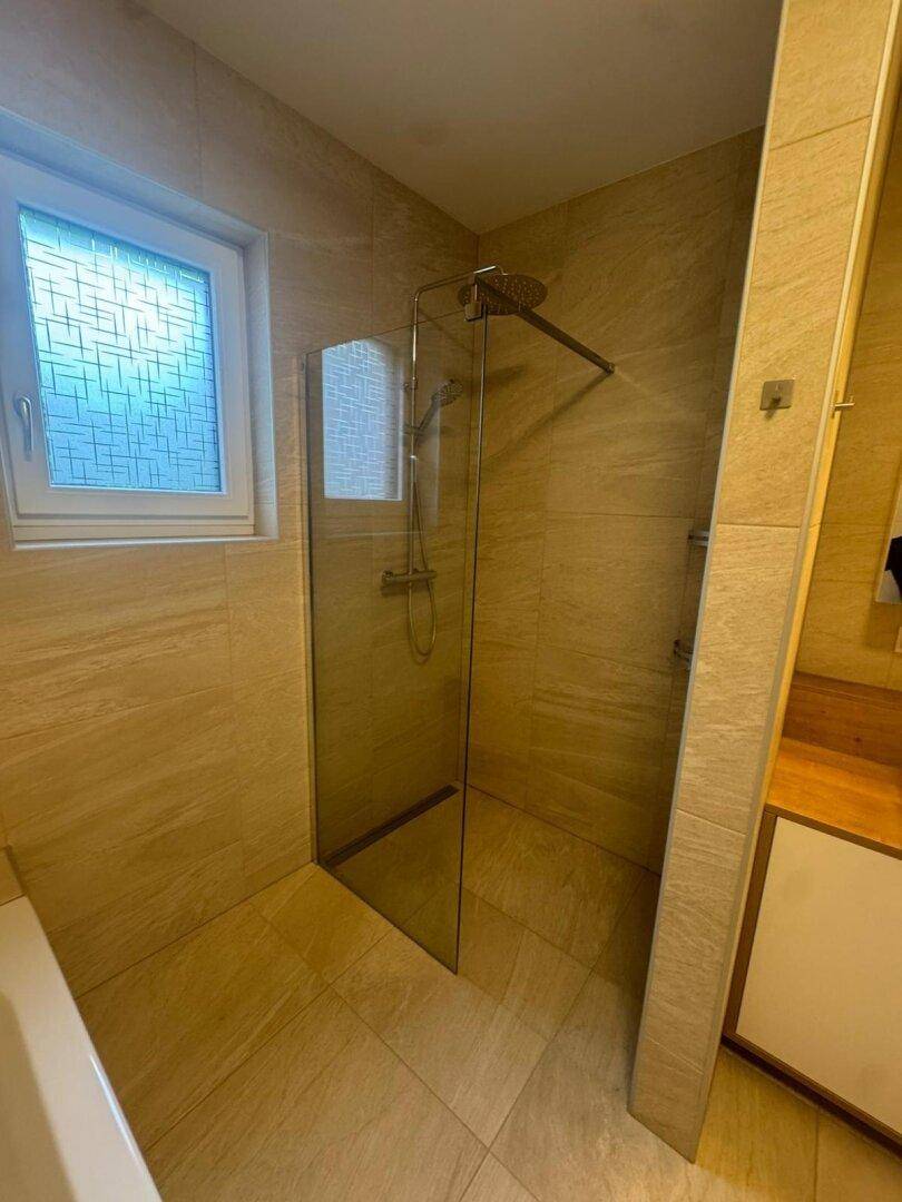 Moderne Duschkabine mit Glasabtrennung und beigefarbenen Fliesen im stilvollen Badezimmer.
