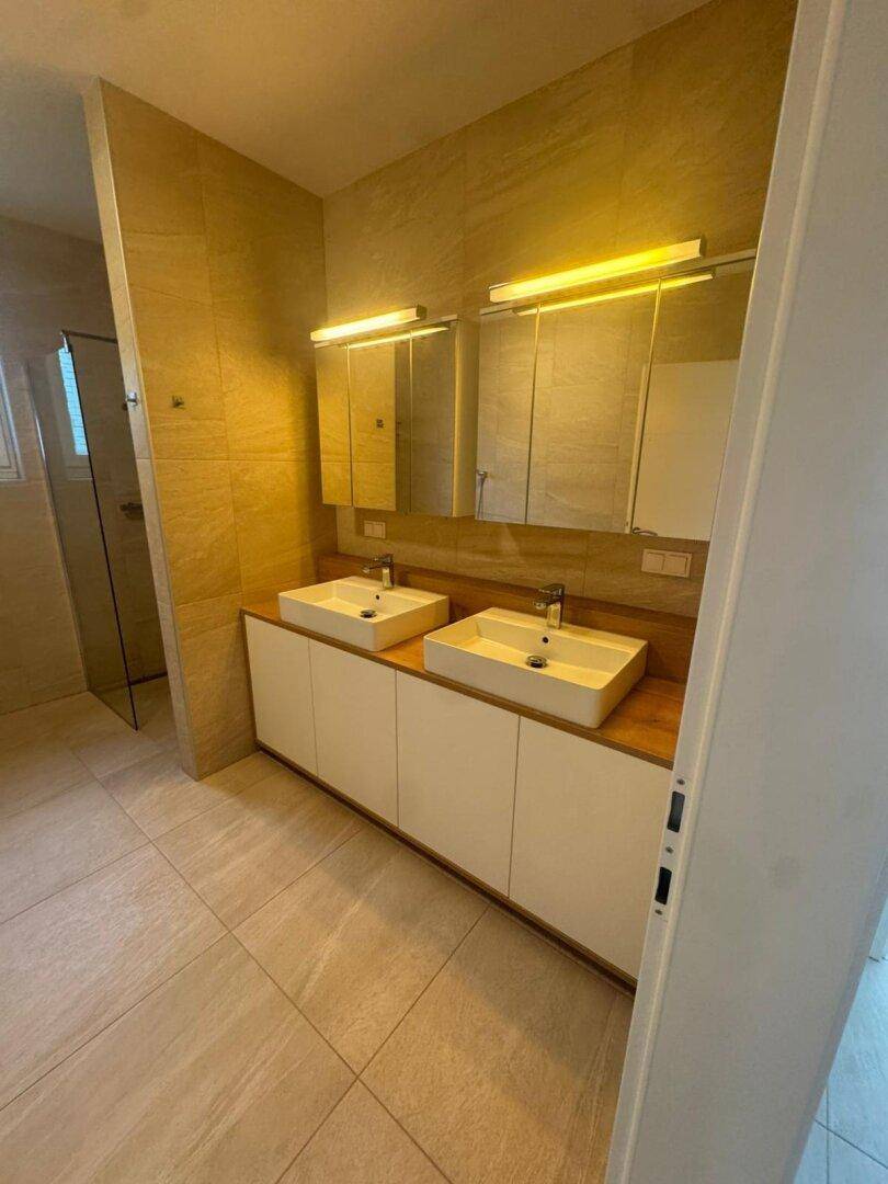 Modernes Badezimmer mit Doppelwaschbecken, großen Spiegelschränken und beigefarbenen Wandfliesen.