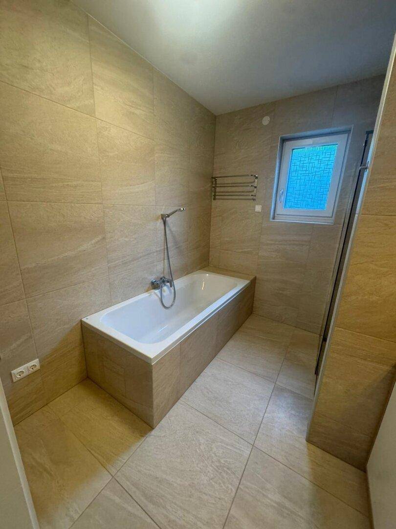 Elegante Badewanne im modernen Badezimmer mit beigefarbenen Fliesen und einem Fenster.