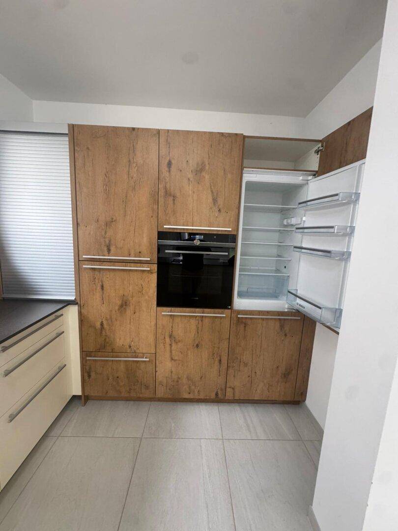 Moderne Küche mit integriertem Backofen und Kühlschrank, ausgestattet mit Holzoptik-Schränken und Fliesenboden.
