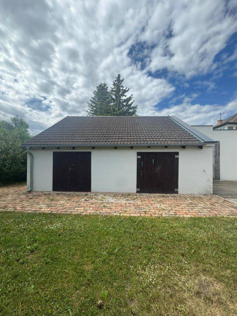 Frontale Ansicht des Garagengebäudes mit zwei Holztoren und Ziegelpflasterung.