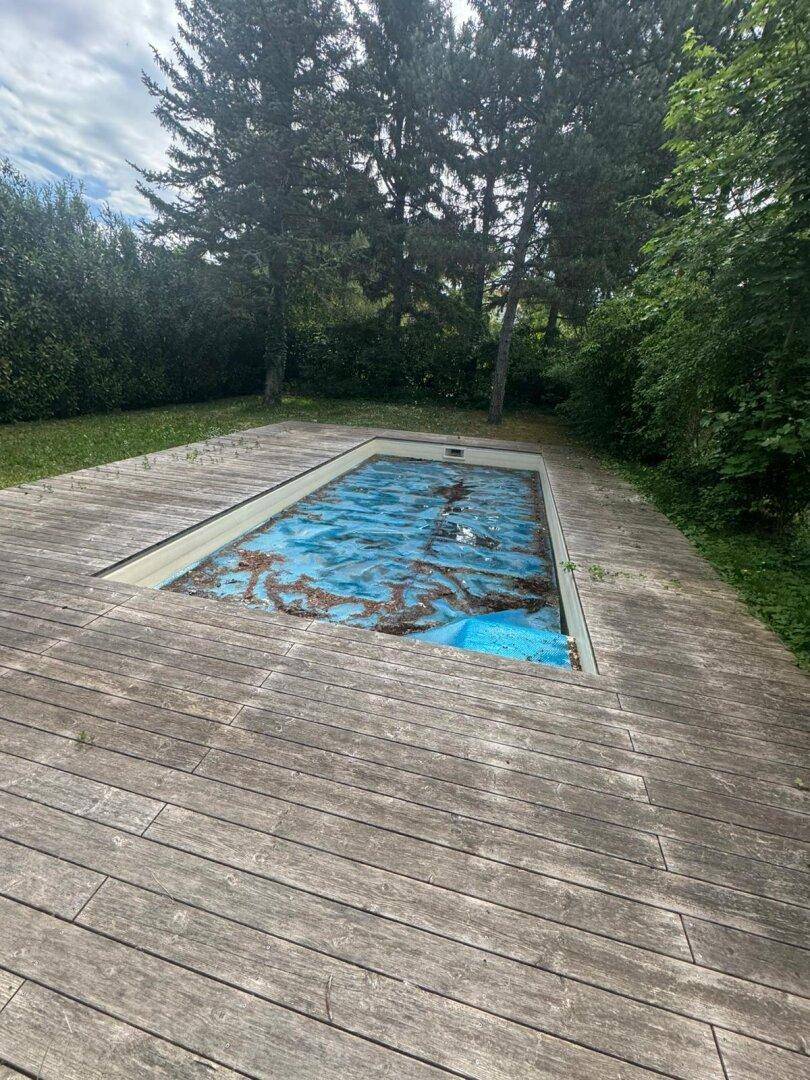 Nahaufnahme des abgedeckten Außenpools mit Holzumrandung im Gartenbereich.