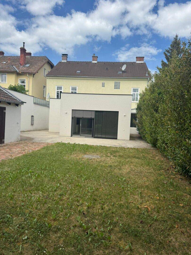 Weitläufiger Gartenbereich mit Rasenfläche und Blick auf das modernisierte Gebäudeensemble.