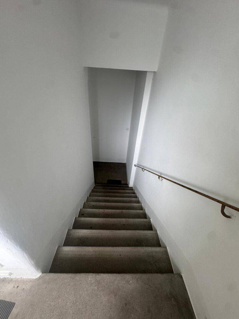 Betontreppe führt hinunter in den Kellerbereich, ausgestattet mit einem einfachen Handlauf.