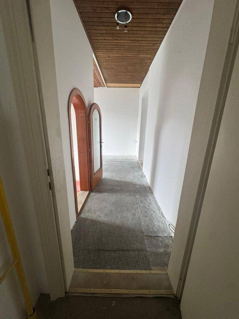 Langer Flur mit Holzpaneeldecke, Teppichboden und charakteristischen Rundbogentüren.