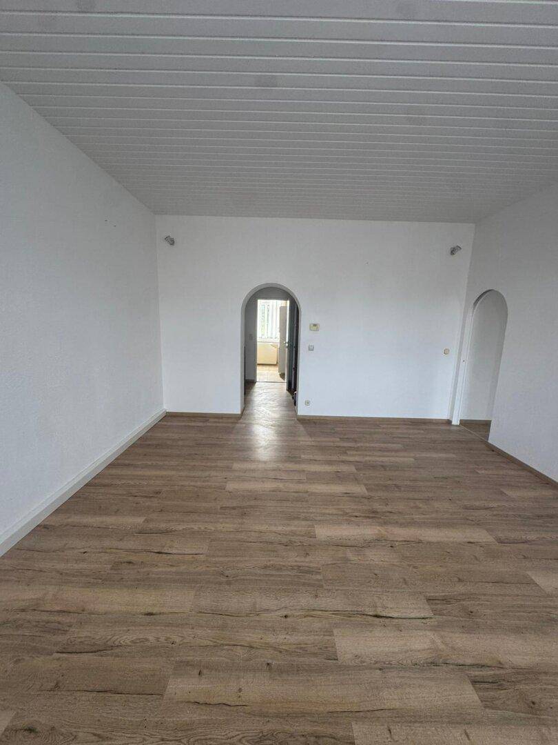 Heller Raum mit Holzboden, weißer Paneeldecke und eleganten Rundbogentüren.