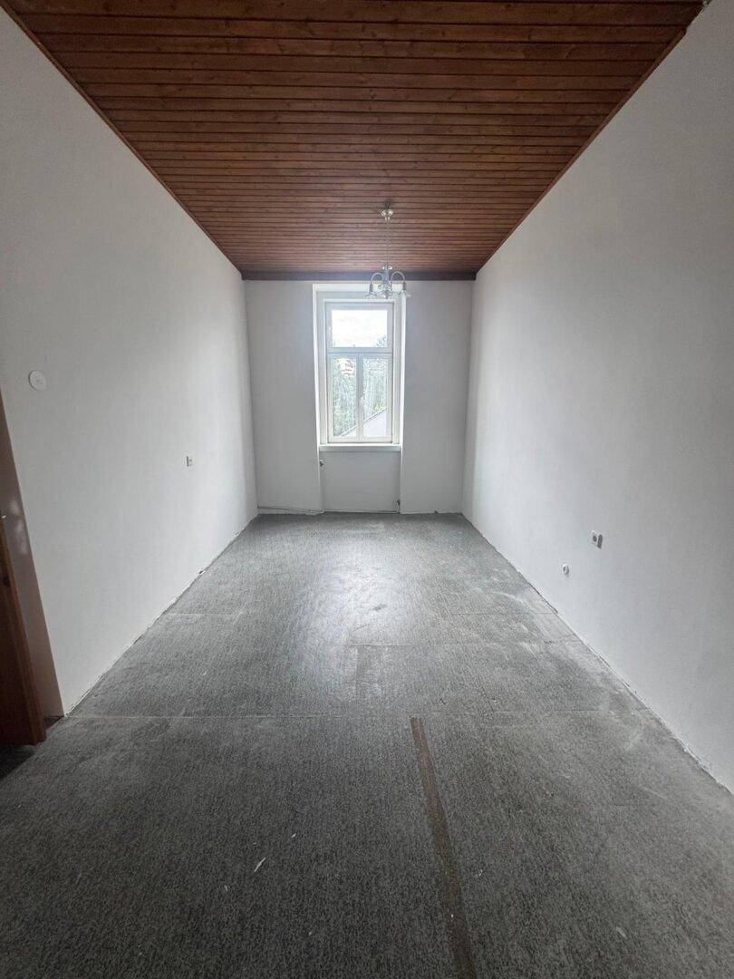 Schmaler Raum mit Teppichboden, Holzpaneeldecke und einem Fenster am Ende des Raumes.