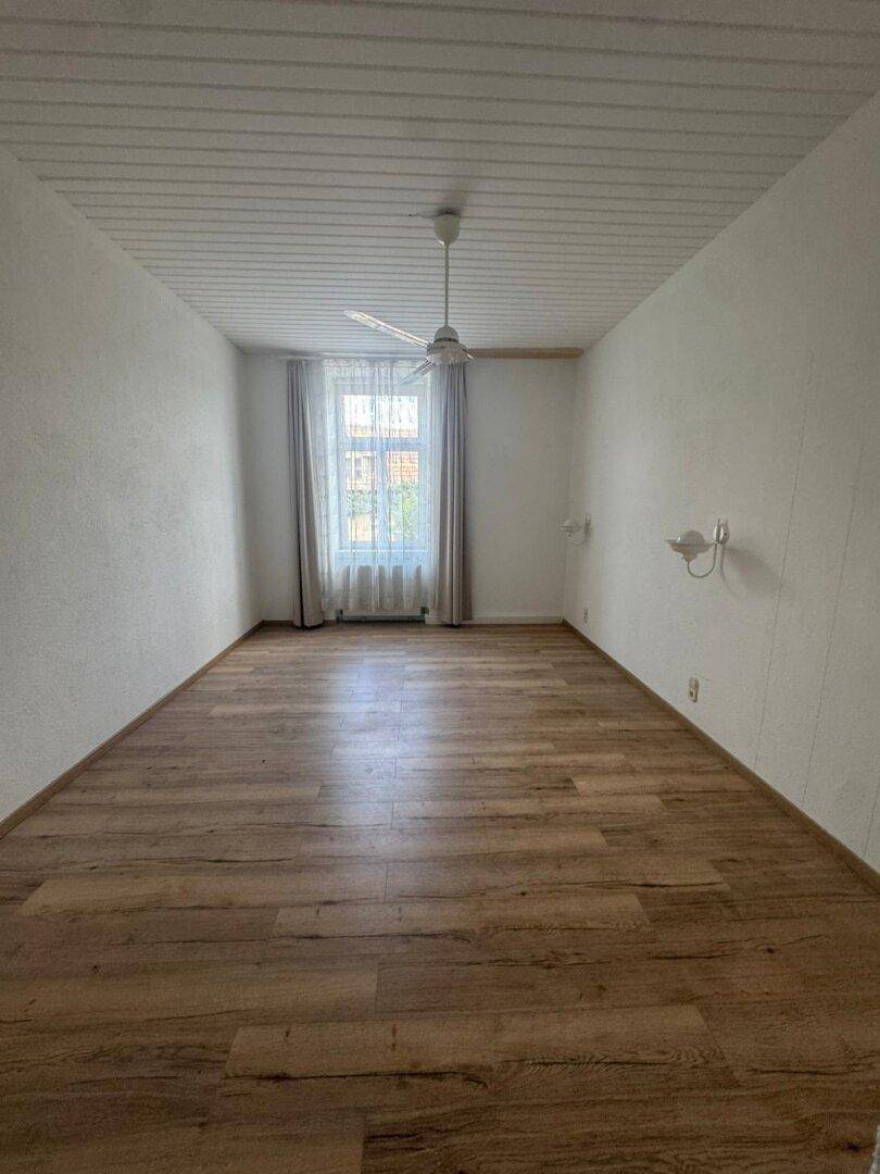 Helles, leeres Zimmer mit Holzdeckenverkleidung, Laminatboden und Deckenventilator, bereit zur Einrichtung.
