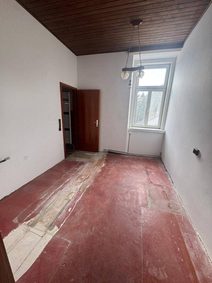 Renovierungsbedürftiges Zimmer mit freigelegtem Boden und dunkler Holzdecke, wartet auf Neugestaltung.