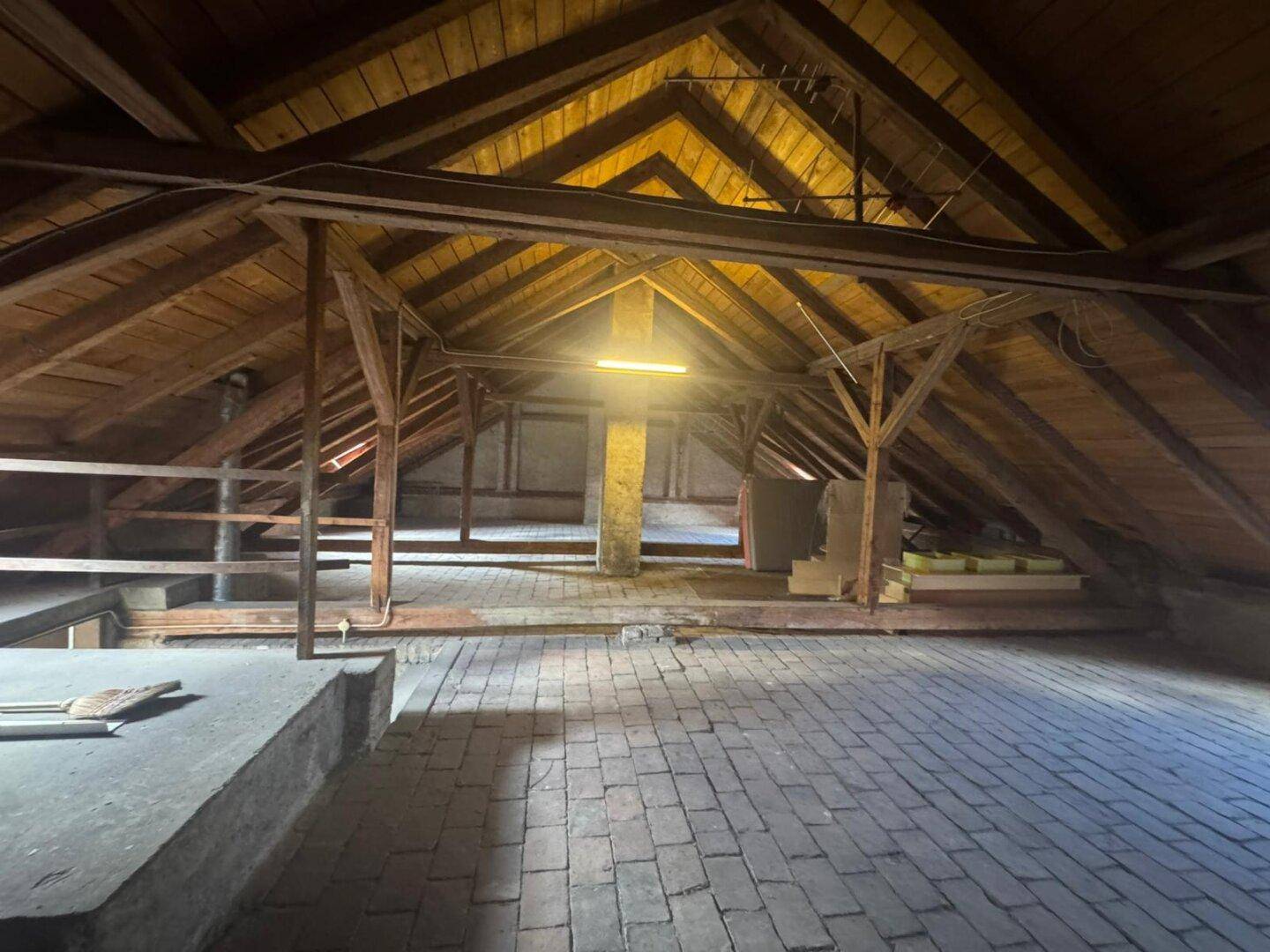 Weitläufiger Dachbodenbereich mit freiliegenden Holzbalken und Ziegelboden, ideal für zukünftigen Ausbau.