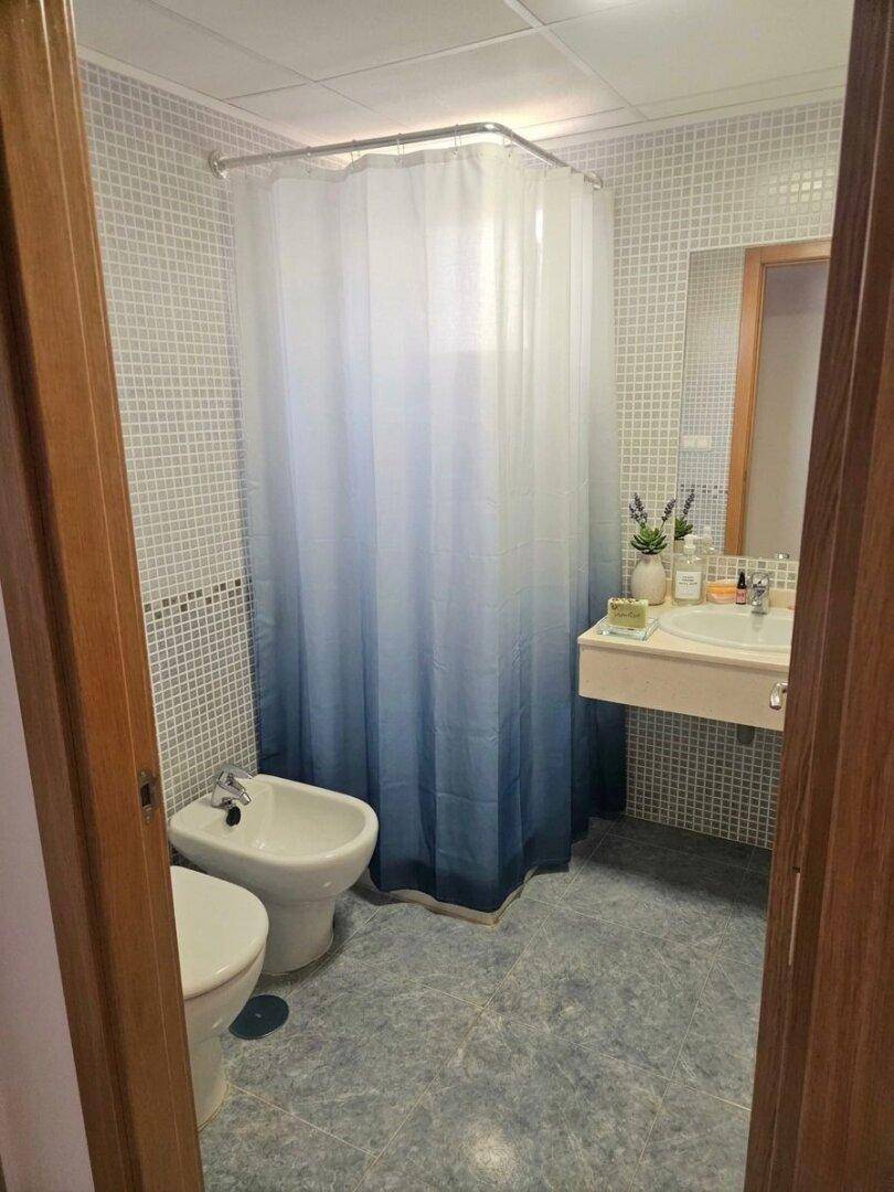 Badezimmer mit blauen Mosaikfliesen, Waschbecken, Bidet und Duschbereich mit Vorhang.