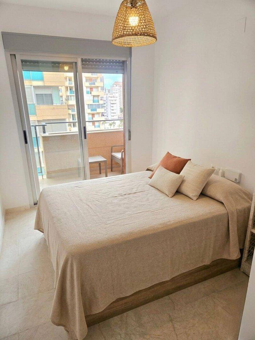 Helles Schlafzimmer mit Doppelbett, Fliesenboden und direktem Zugang zu einem Balkon.