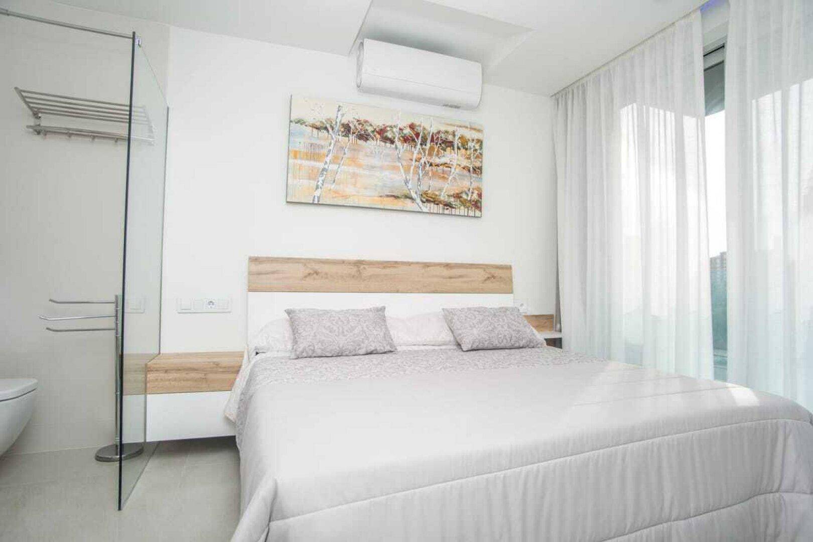 Schlafzimmer mit Klimaanlage, großen Fenstern und Vorhängen für viel Tageslicht.