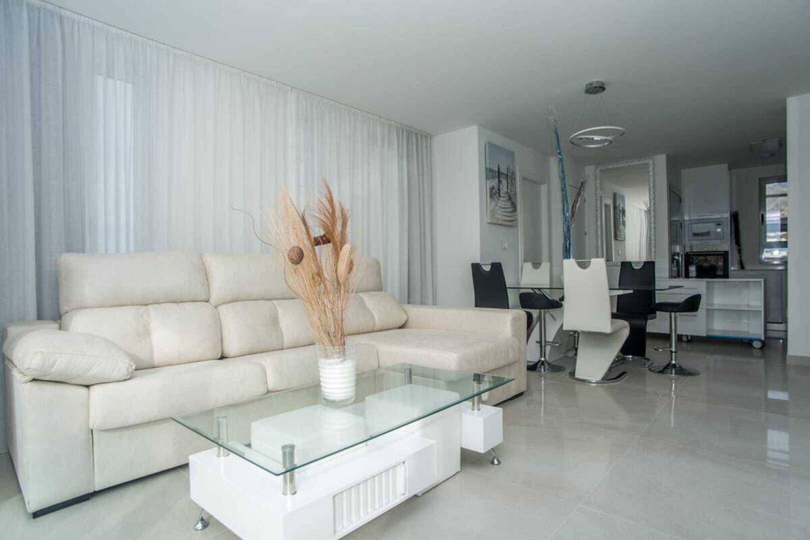 Geräumiger Wohn-Essbereich mit beigem Sofa, Glastisch und Blick auf die offene Küche.