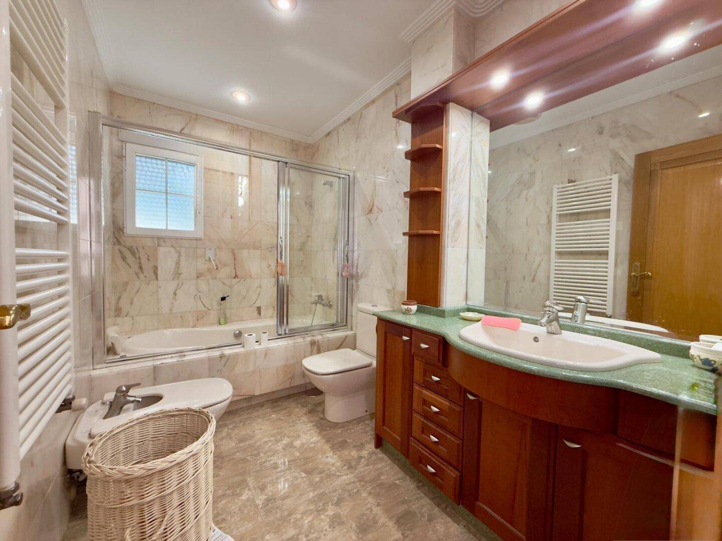 Elegantes Badezimmer mit Marmorfliesen, Badewanne, Bidet und einem Holzwaschtisch.