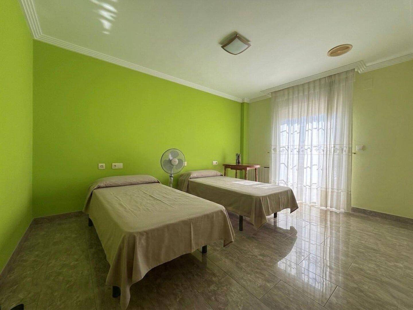 Helles Schlafzimmer mit zwei Einzelbetten, grünen Wänden und Fliesenboden.