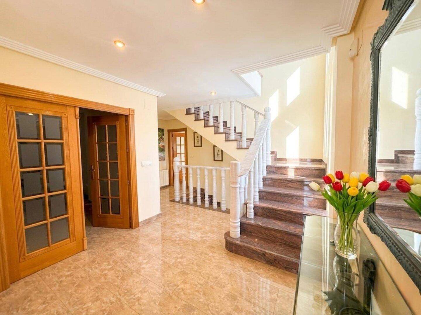 Heller Flur mit eleganter Marmortreppe und dekorativem Spiegel.