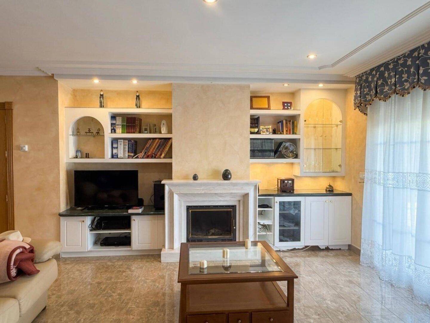 Gemütliches Wohnzimmer mit Kamin, Einbauregalen und glänzenden Fliesenböden.