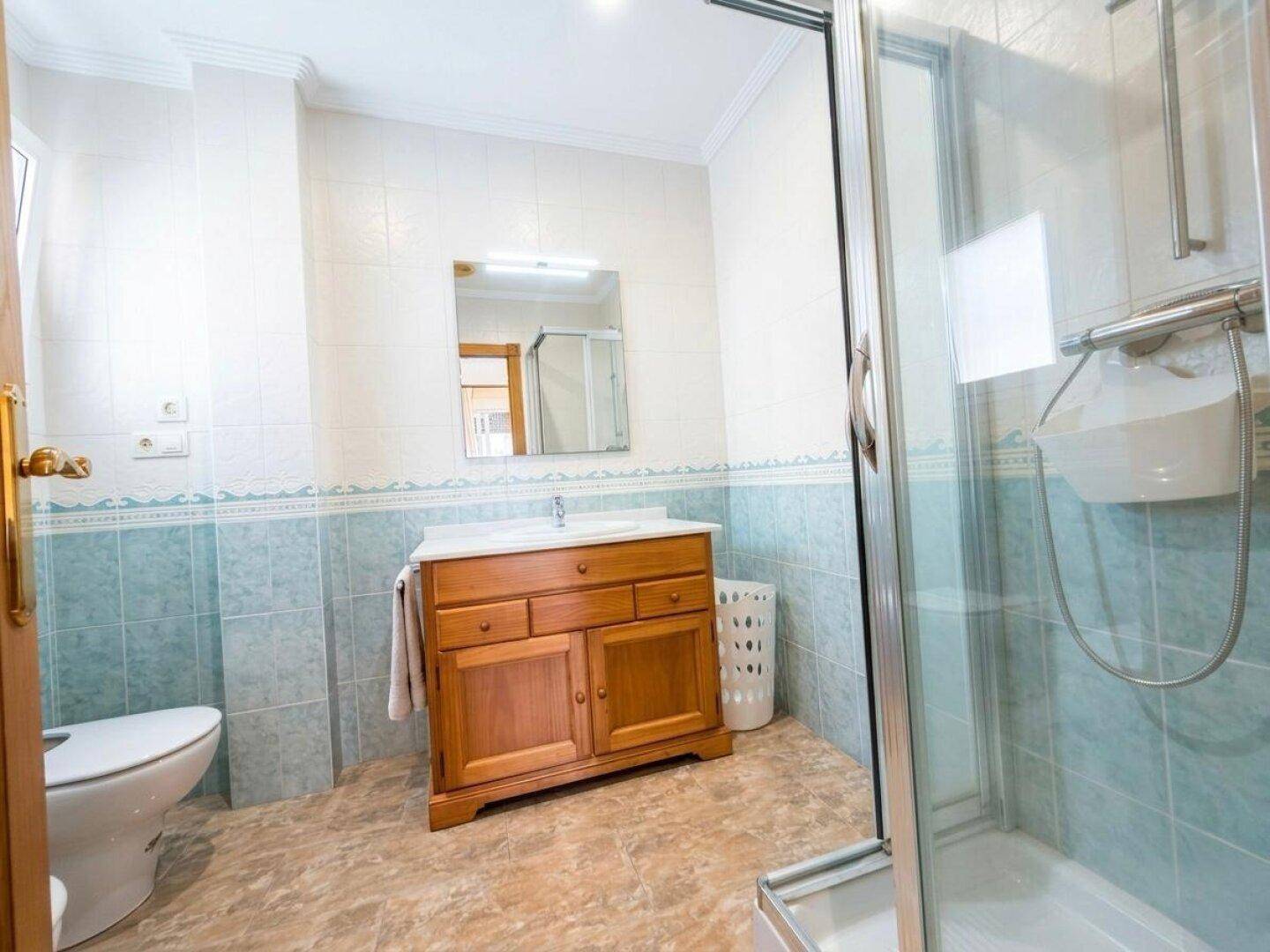 Badezimmer mit Duschkabine, WC und Holzwaschtisch, dekoriert mit blauen Fliesen.