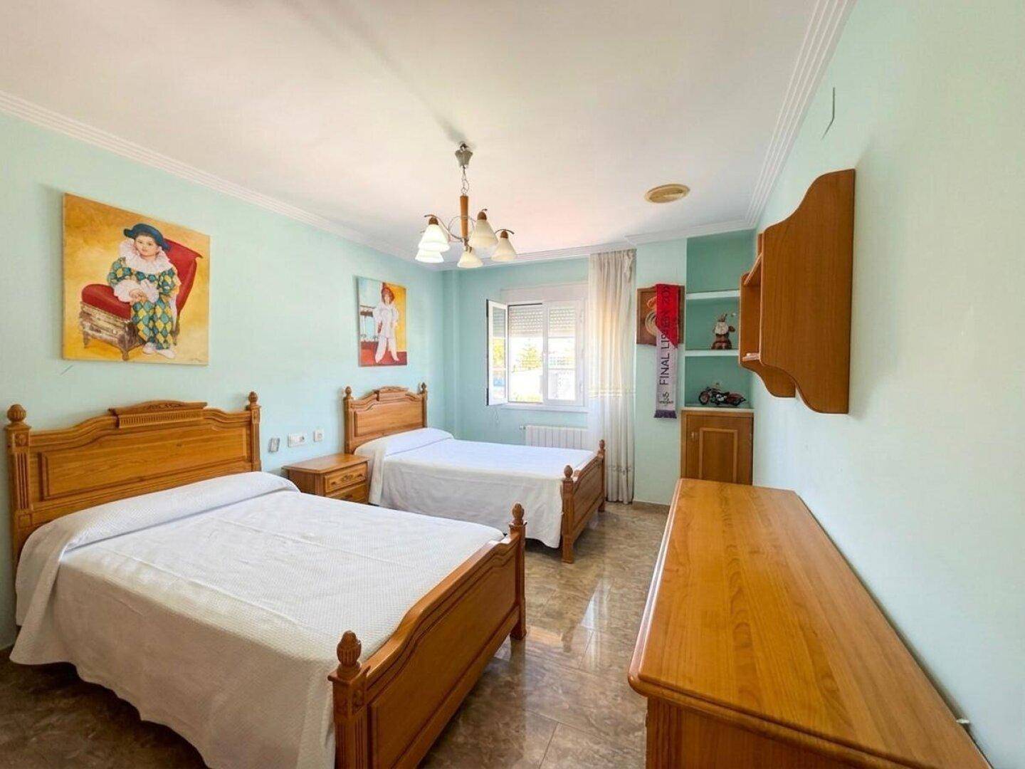 Freundliches Schlafzimmer mit zwei Einzelbetten, Holzmöbeln und hellgrünen Wänden.