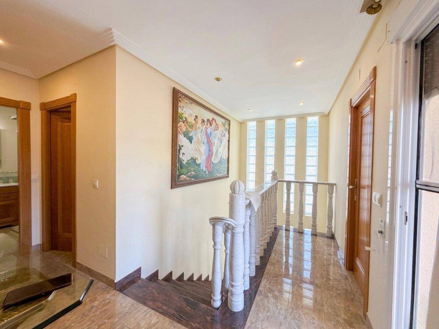 Heller Flur mit Treppe, Fliesenboden und dekorativem Gemälde an der Wand.