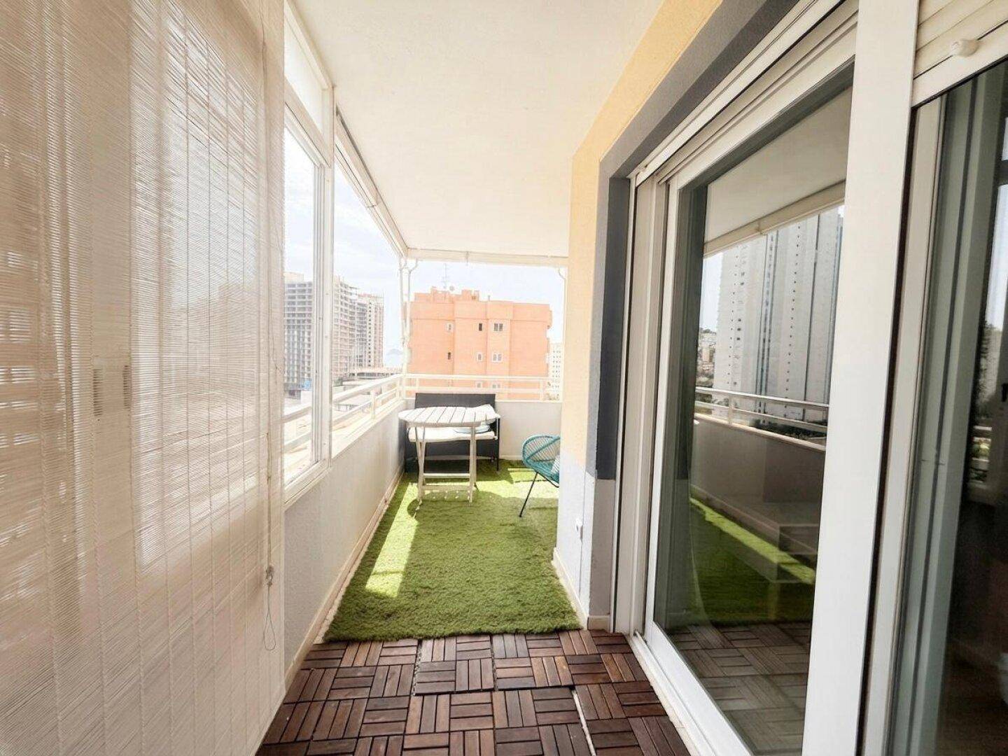 Langer Balkon mit Kunstrasen und Holzdielen, der einen Blick auf die umliegenden Gebäude bietet.