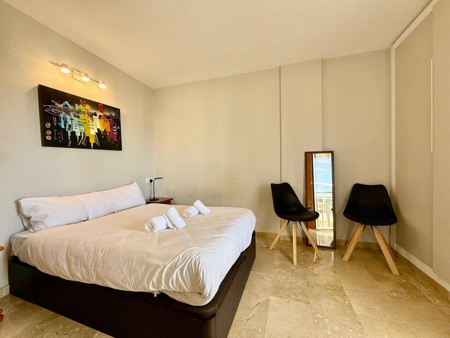 Schlafzimmer mit Doppelbett, modernem Kunstwerk und Fliesenboden.