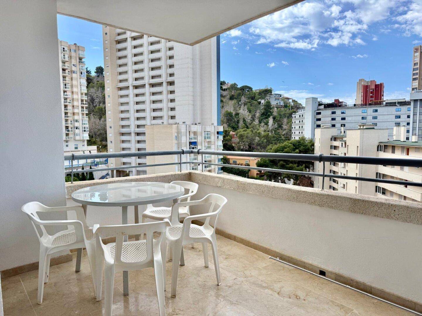 Heller Balkon mit Sitzgelegenheiten und Ausblick auf die umliegenden Gebäude und grünen Hügel.