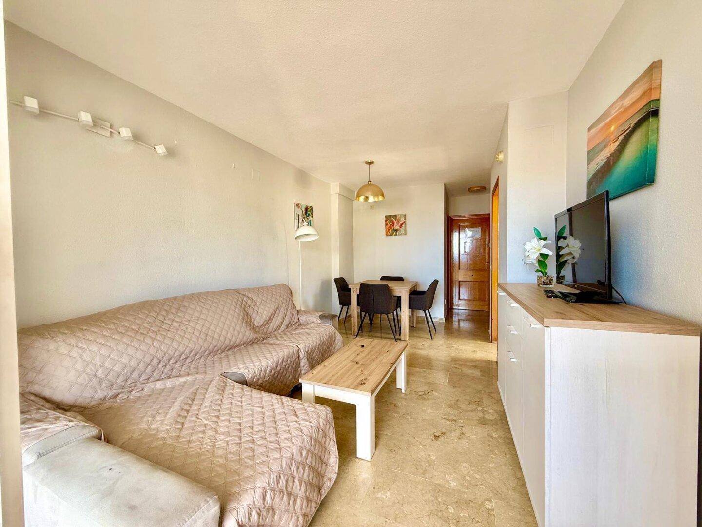 Heller Wohn- und Essbereich mit beigem Sofa, Esstisch und Fliesenboden.