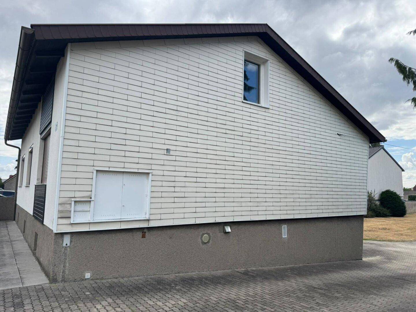 Seitenfassade des Hauses mit weißer Verkleidung und einem Fenster im Obergeschoss.