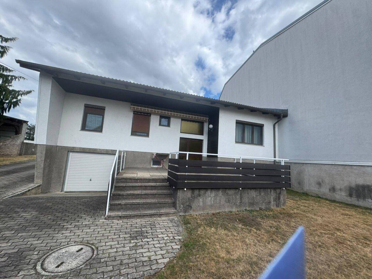 Hausfassade mit Außentreppe zum Eingang und einer Garage im Untergeschoss.