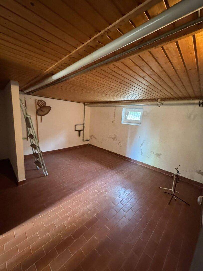 Kellerraum mit Holzdecke, Fliesenboden und einem kleinen Fenster für Tageslicht.