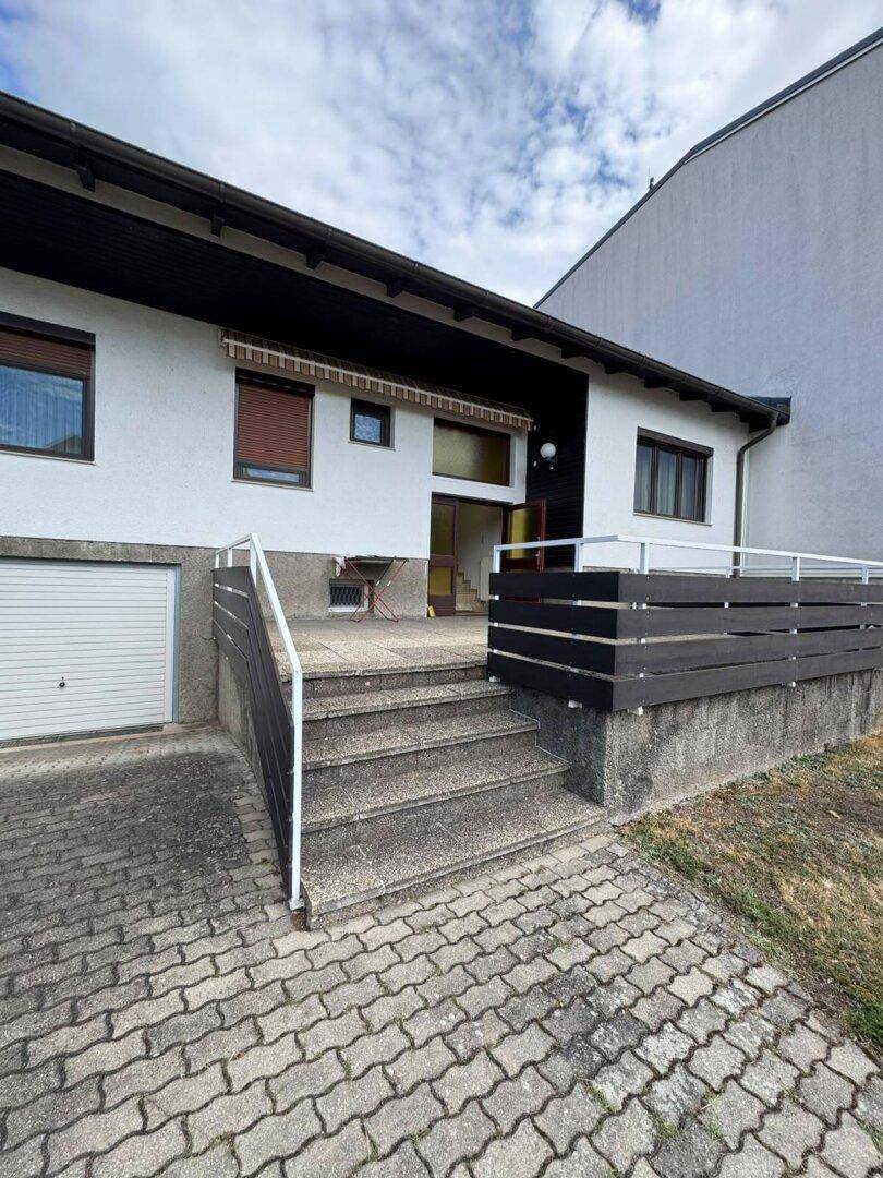 Außentreppe führt zum Hauseingang mit einer kleinen Terrasse und Geländer.