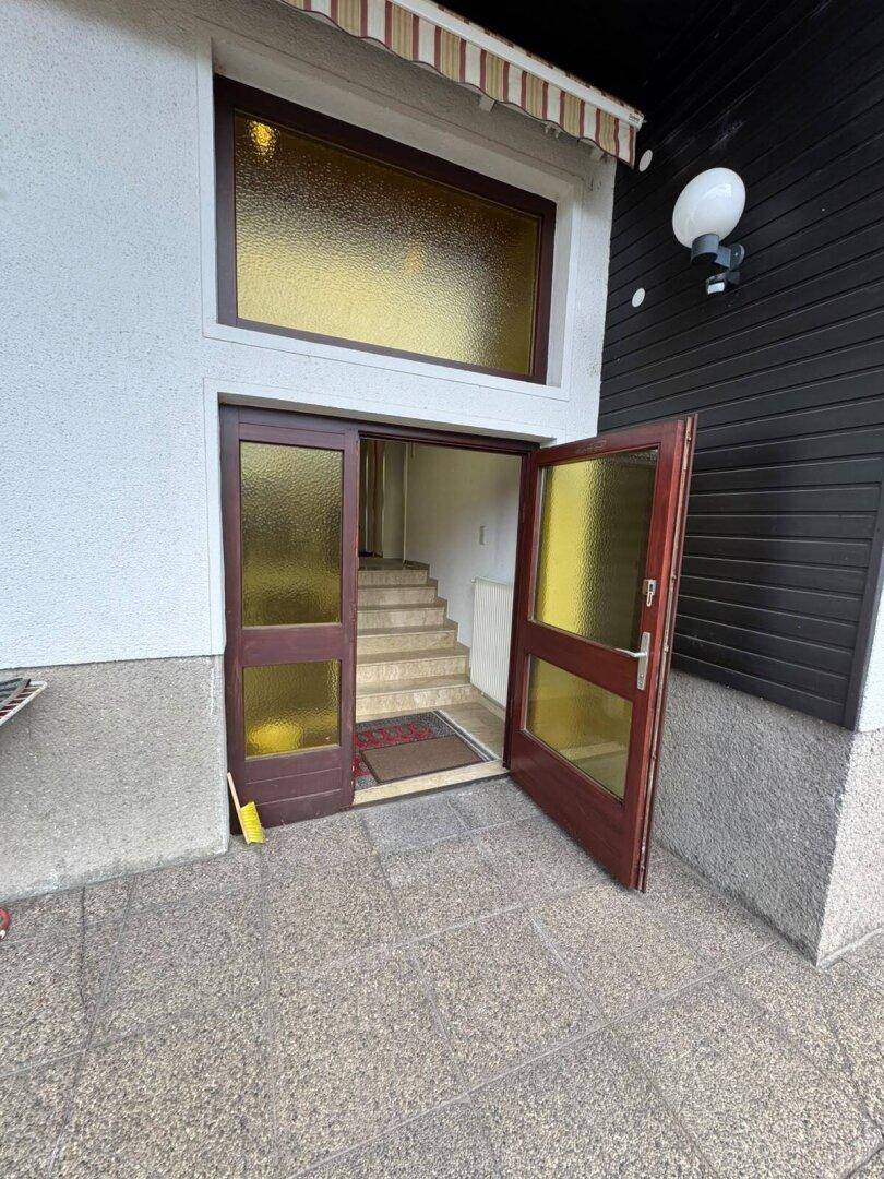 Eingangsbereich mit offener Holztür, die zu einer Treppe ins Innere führt.