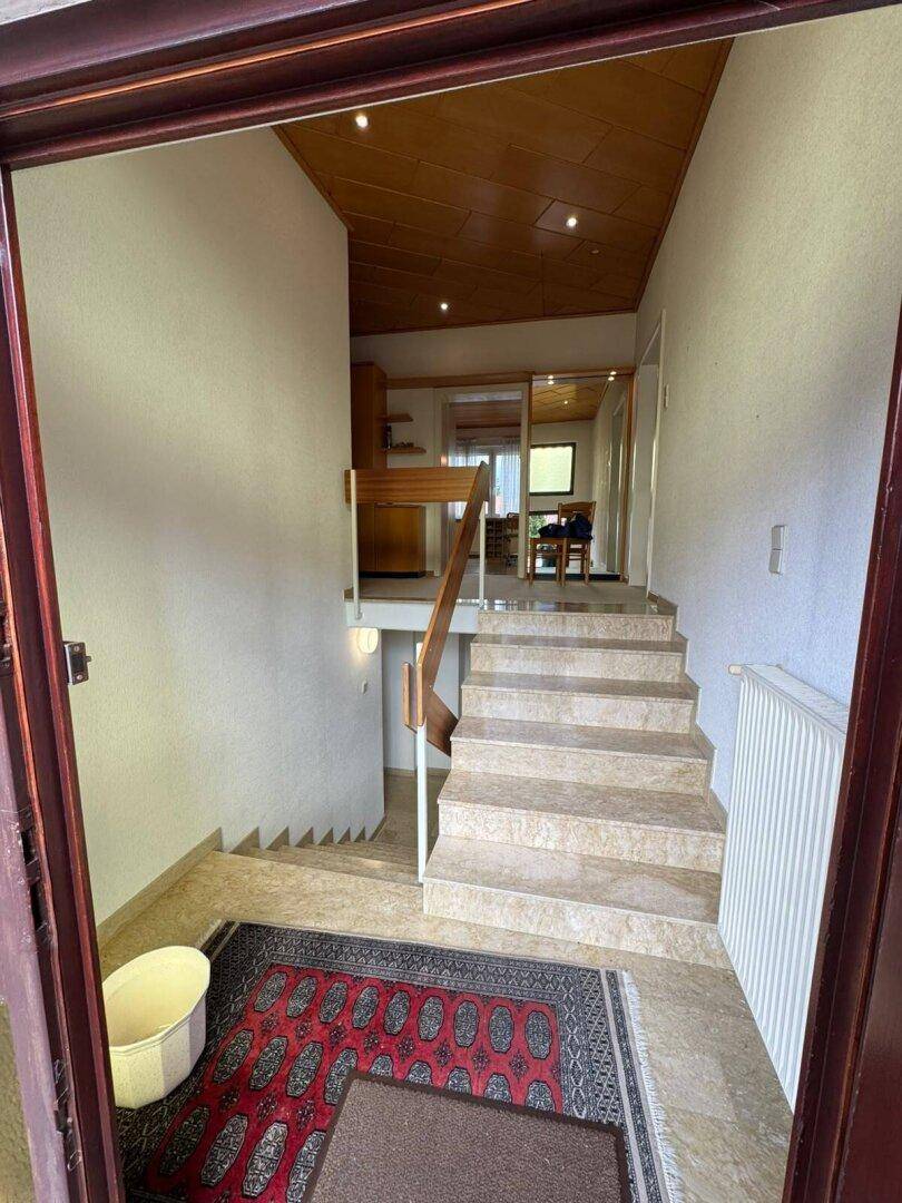 Heller Eingangsbereich mit Marmorboden, Holzdecke und Treppe zu den oberen Etagen.