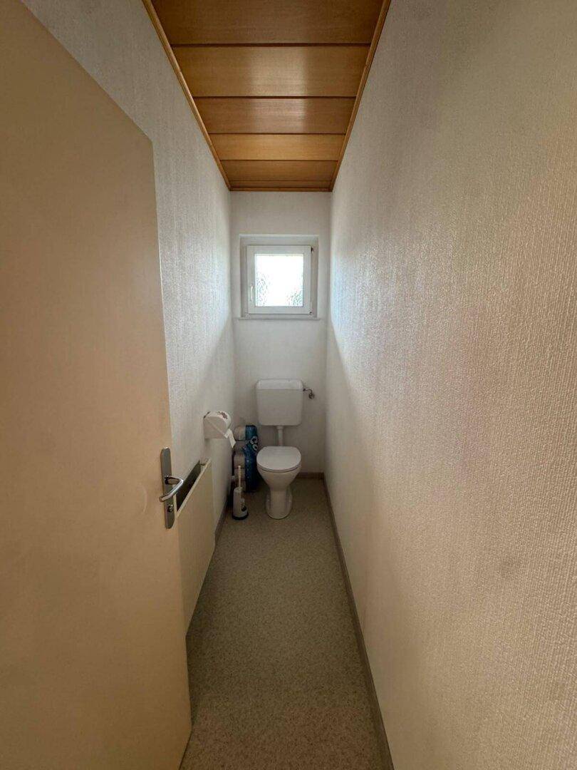 Kleines Gäste-WC mit Fenster, Toilette und einfacher Ausstattung.