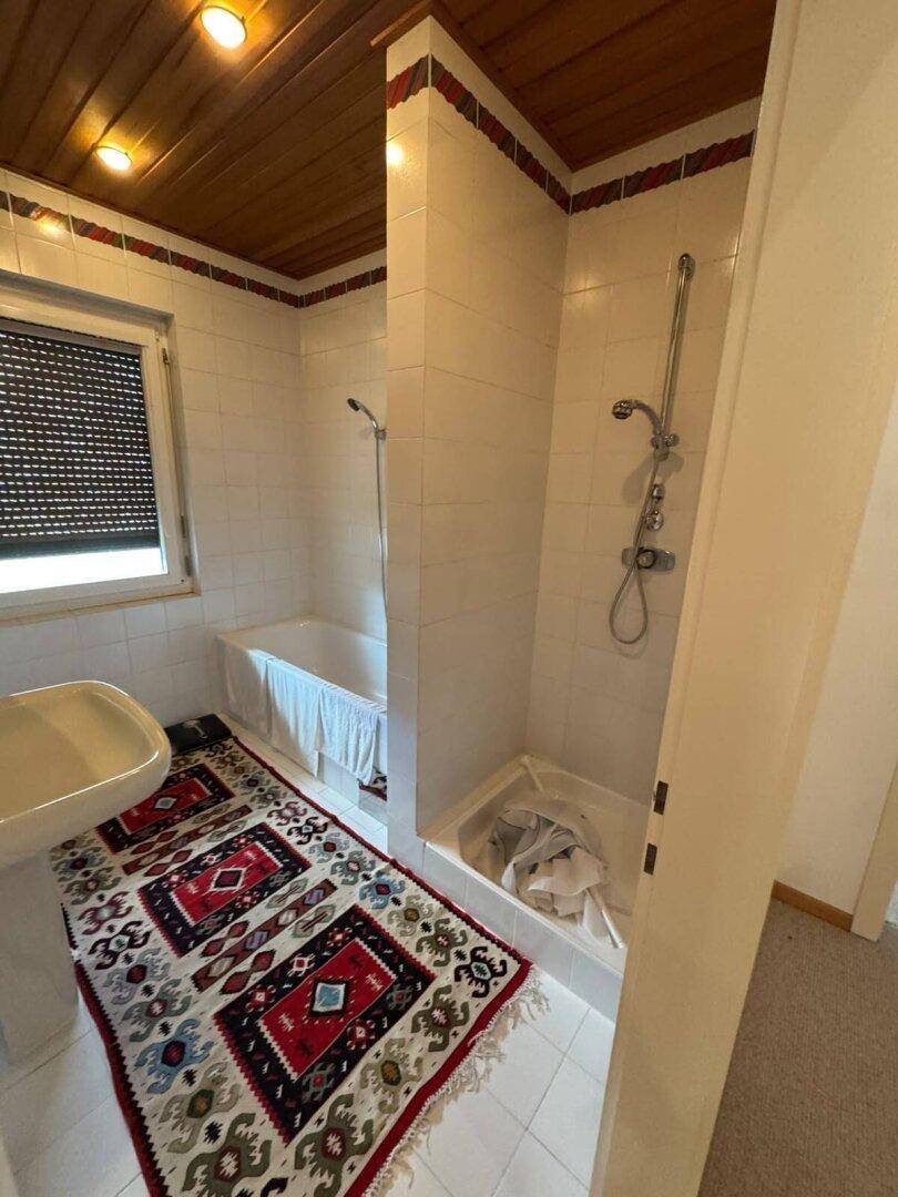 Badezimmer mit Badewanne, Dusche und Waschbecken, ausgestattet mit Fliesen und Holzdecke.