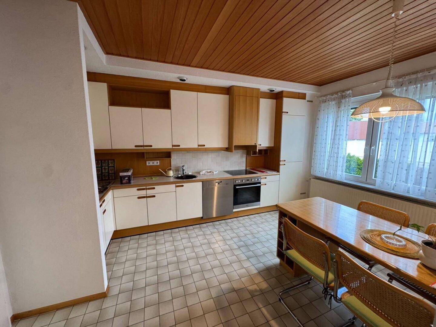 Funktionale Küche mit weißen Schränken, Fliesenboden und Essbereich am Fenster.