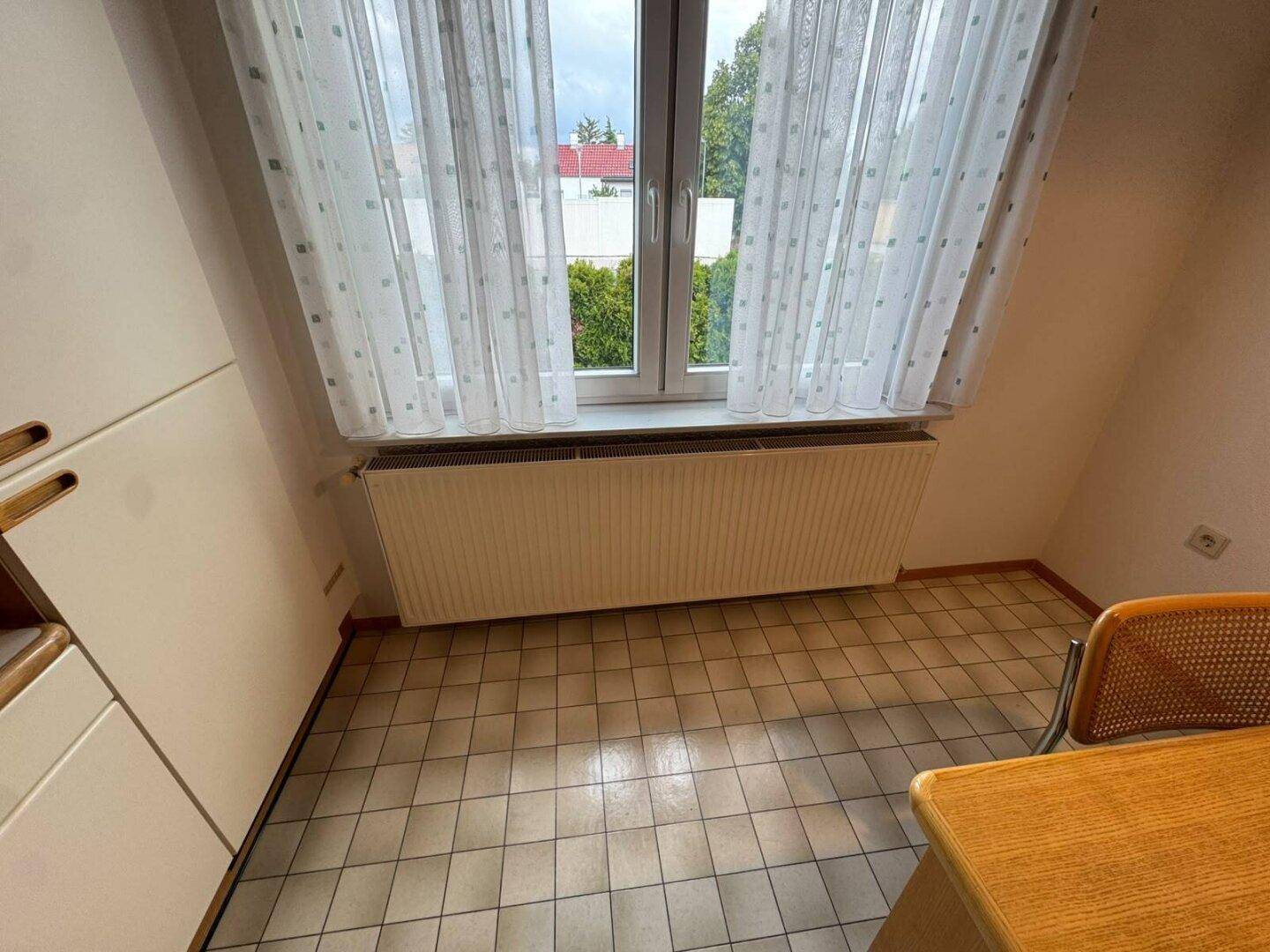 Küchenfenster mit Vorhängen und Heizkörper darunter, bietet Blick ins Grüne.