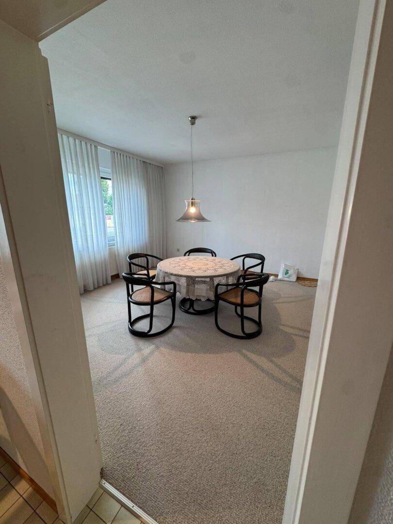 Esszimmer mit rundem Tisch und Stühlen, durch große Fenster gut beleuchtet, mit Teppichboden.