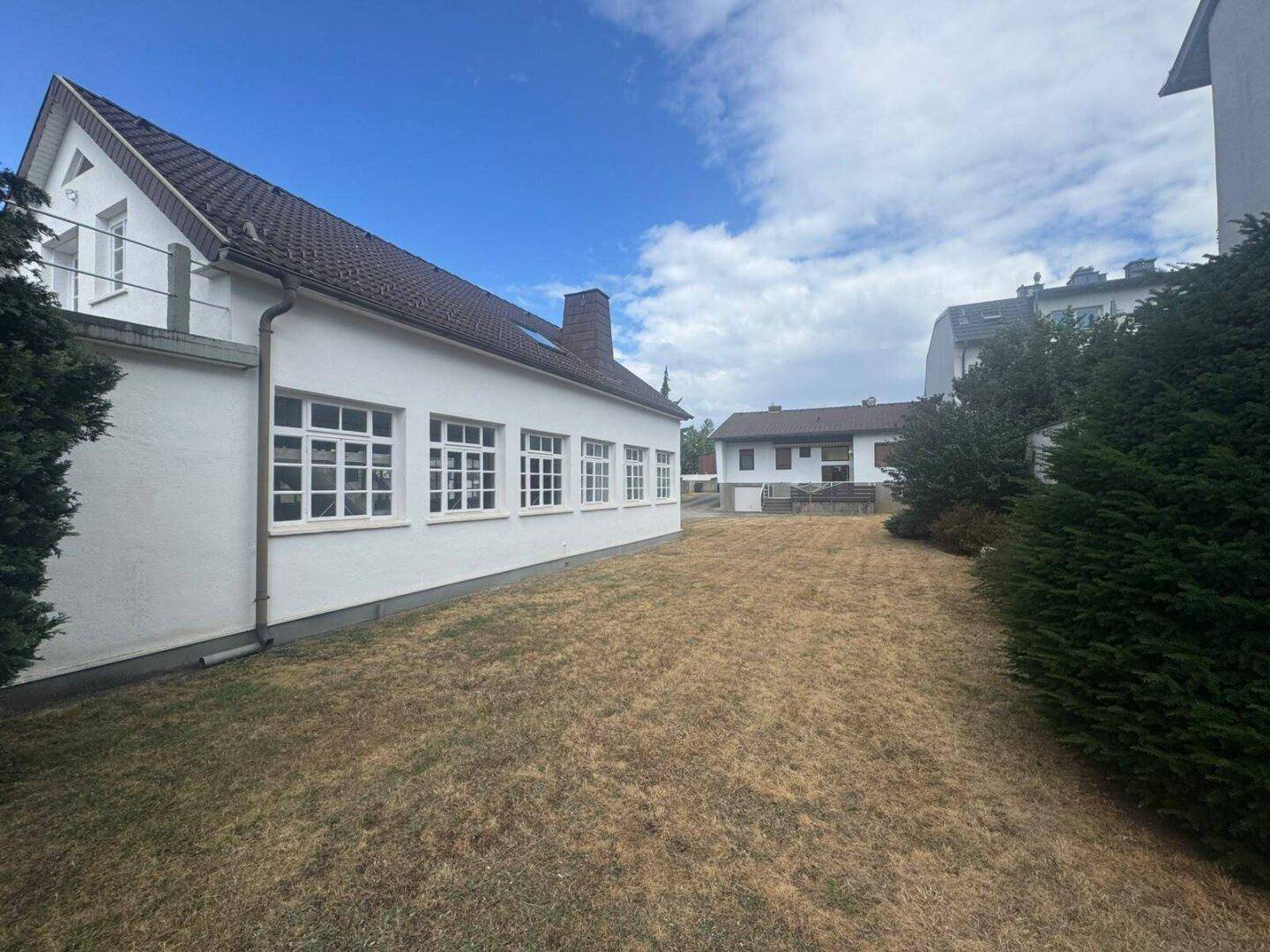 Seitenansicht des Gebäudes mit Fenstern und Schornstein, Blick auf den Garten und Nachbarhäuser.
