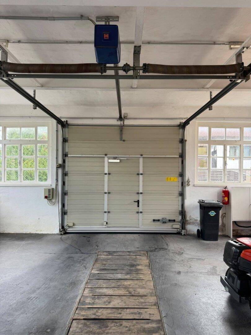 Geräumige Garage mit großem Rolltor, Fenstern und Betonboden, ideal für Fahrzeuge oder Werkstatt.