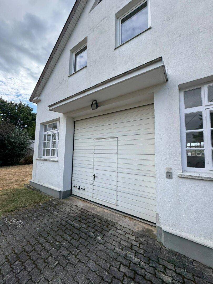 Nahaufnahme des Garagentors und eines Fensters an der Hausfassade, mit Vordach.
