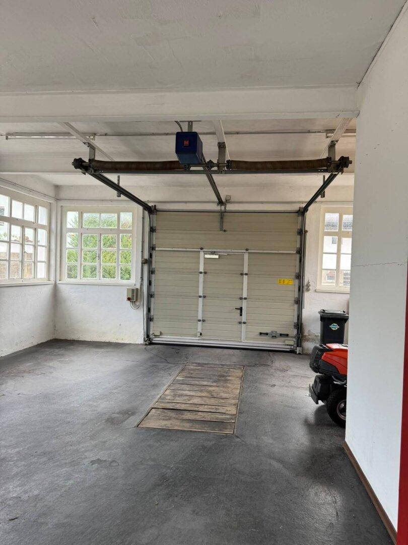 Innenansicht der Garage mit Rolltor, Fenstern und viel Platz, geeignet als Arbeitsbereich.
