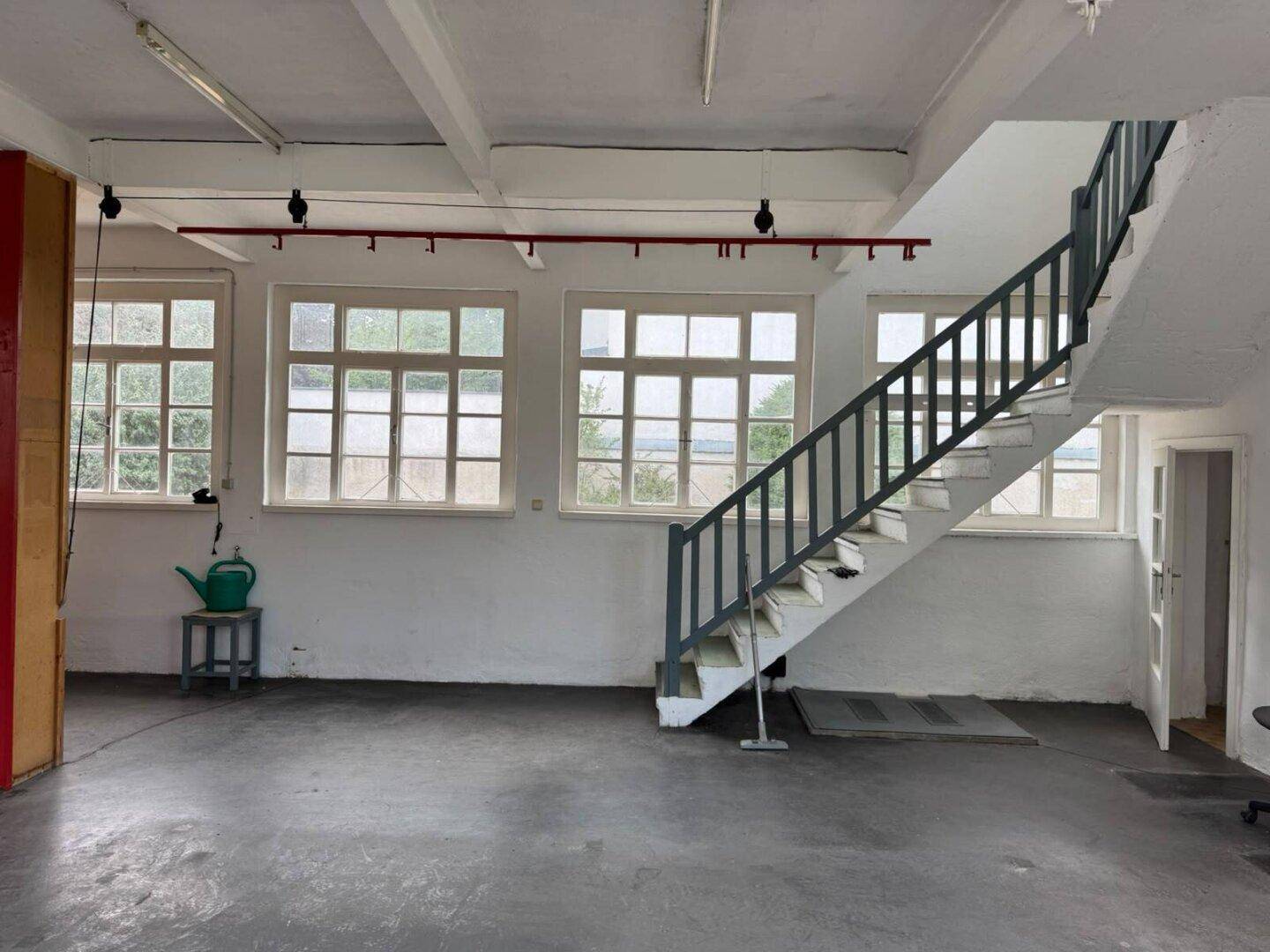Heller Werkstattraum mit Betonboden, Treppe und vielen Fenstern, gut beleuchtet.