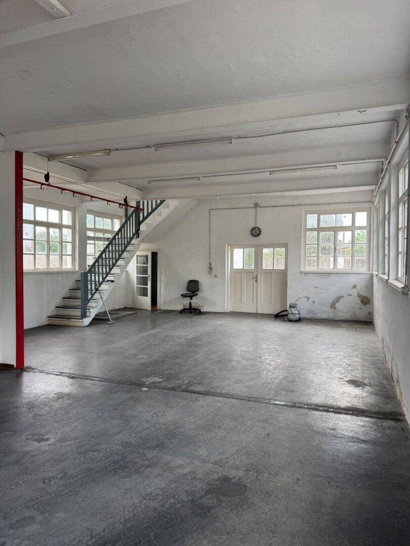 Geräumiger Arbeitsbereich mit Betonboden, Treppe und großen Fenstern, bietet viel Licht.