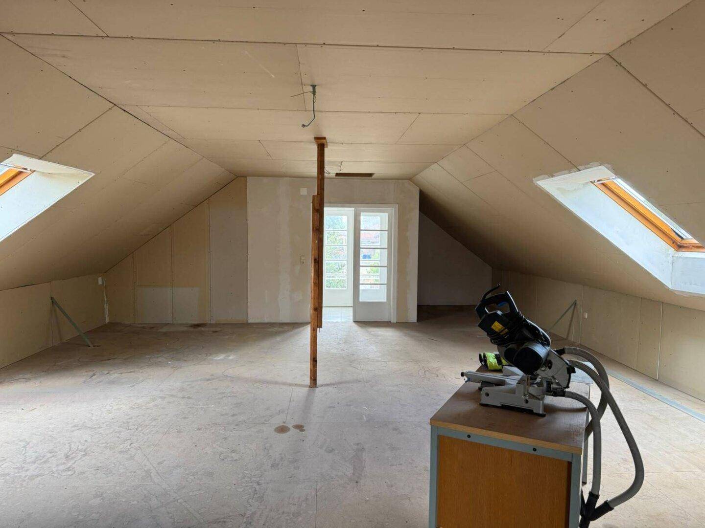 Weiterer Blick in den unausgebauten Dachboden mit Holzbalken, Dachfenstern und Tür.